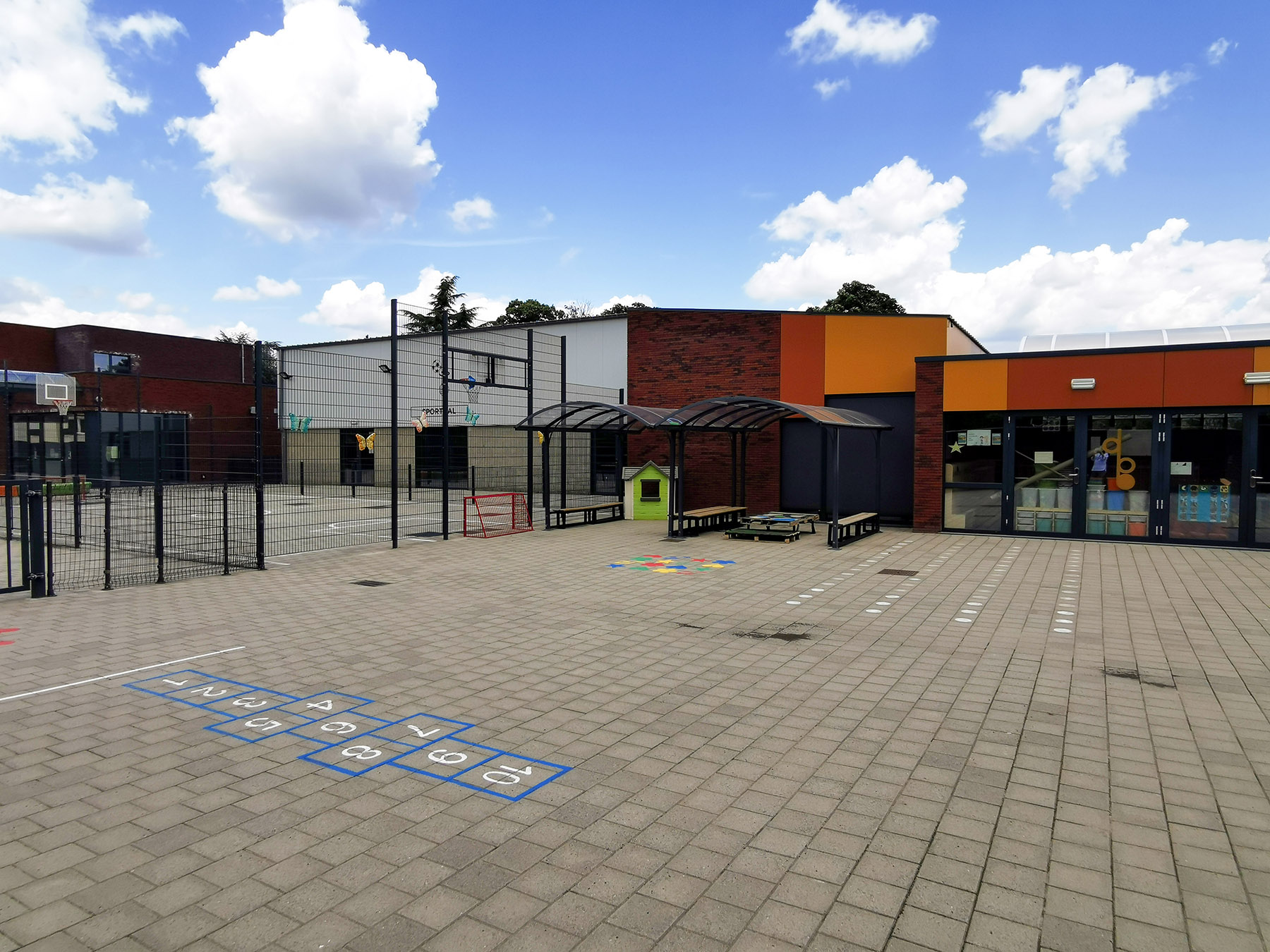 Speelplaats met hinkelspel, speelhuisje en zicht op de klaslokalen