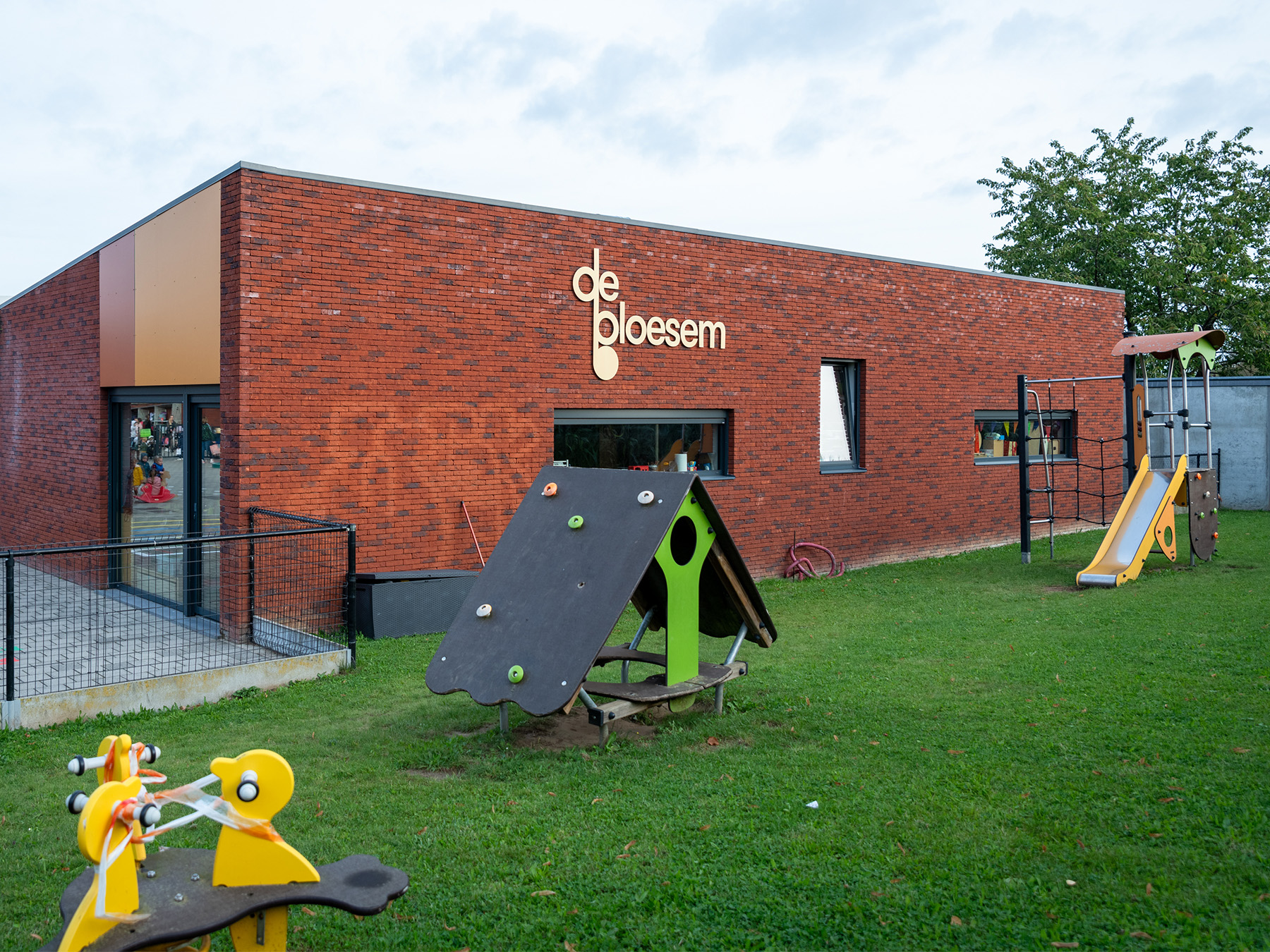 Speelplaats met klimtoestel en glijbaan tegen de rode gevel van de school