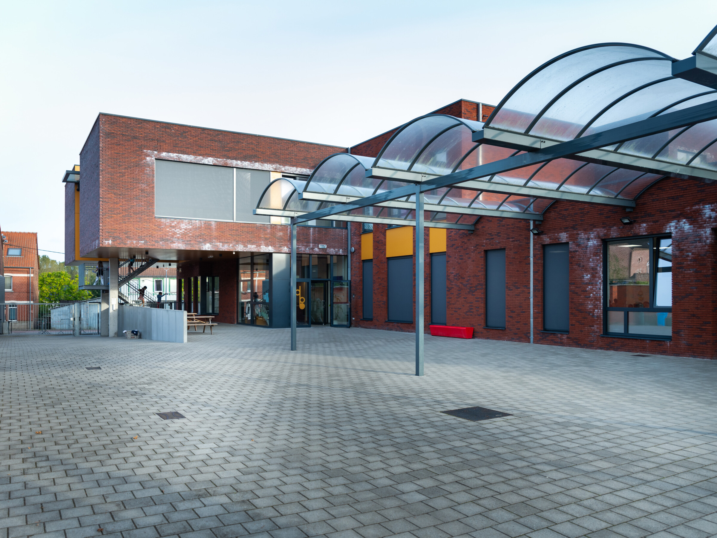 Overdekte inkomhal met glazen luifel aan de schoolingang