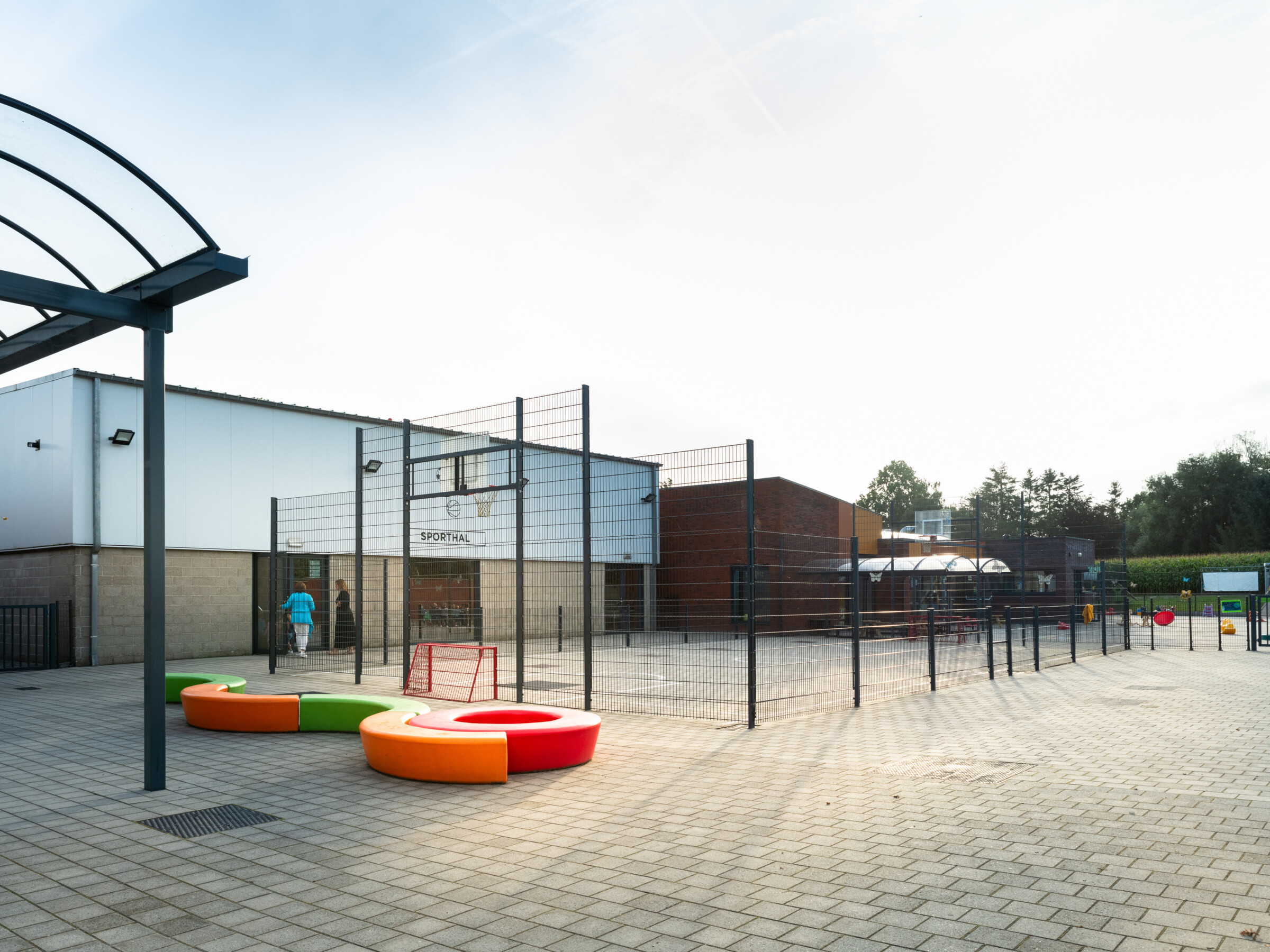 Omheind sportterrein met basketbalring naast de sporthal